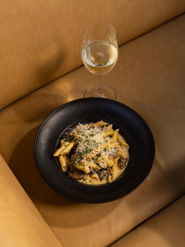 A bowl of pasta and white wine in a booth