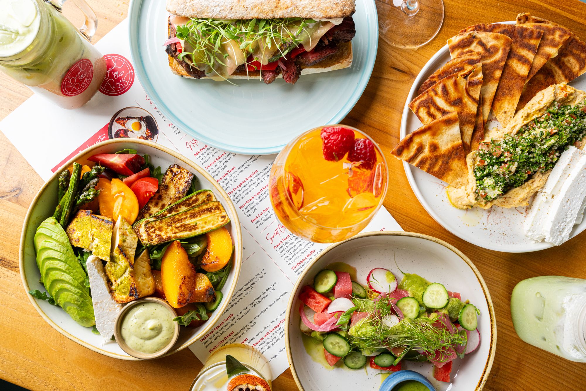Overhead spread of plated dishes, salads and a cocktail on a restaurant table